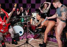Rock n' roll conjures a raunchy spirit, and Filou seamlessly flips Kona from a standing 69 to cock-bouncing enthusiastically on the stool to eating her ass from the back -- crazy style! The live debauchery has Abby horned up, too, rubbing her pussy while the other band members catch wise and cheer them on. Filou leads the number to a cum-n-cymbal crashing finish, and the rockers play on.